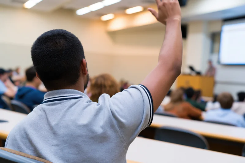 Student raising hand in classroom lecture setting