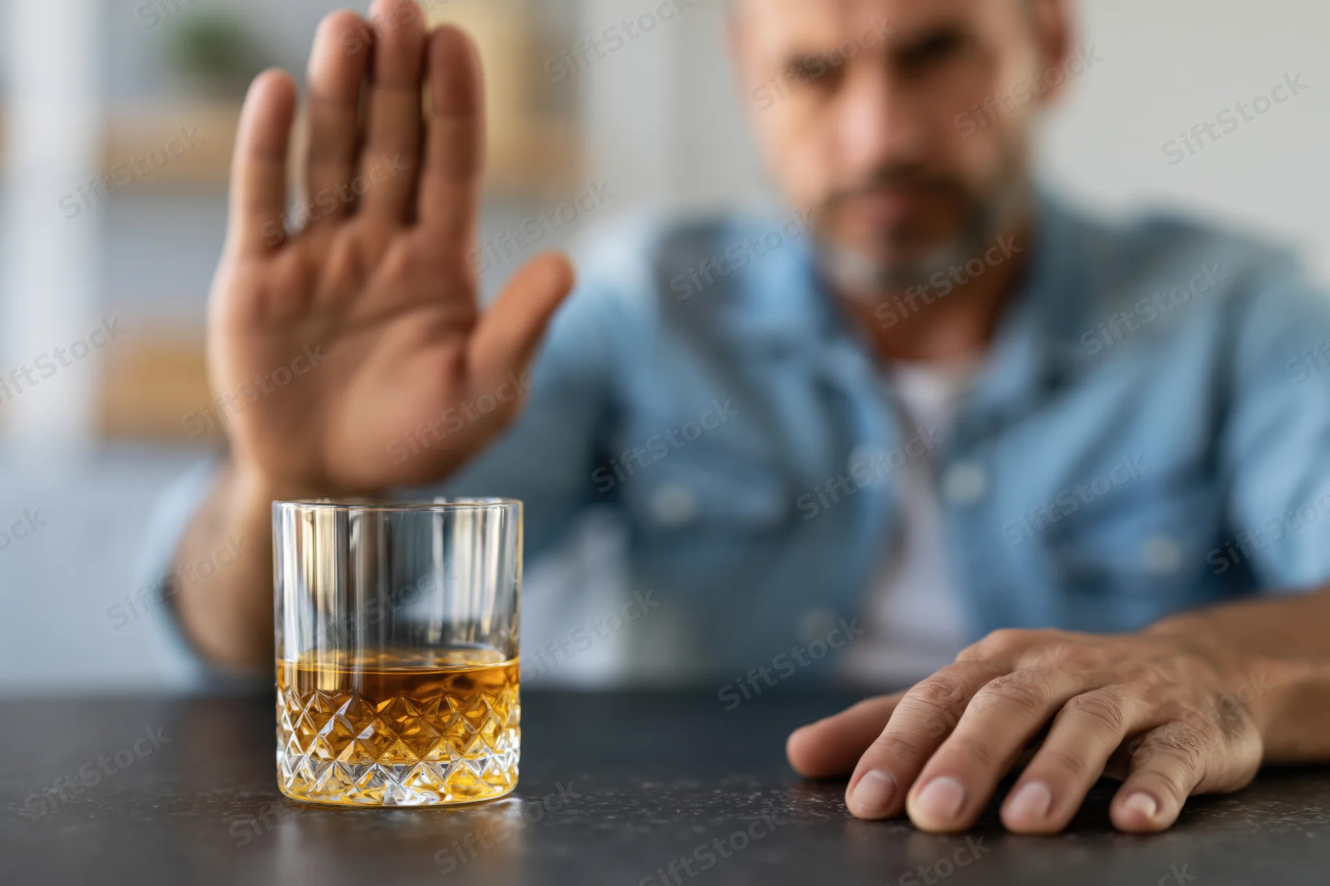 Man raising hand in refusal toward whiskey glass on dark table