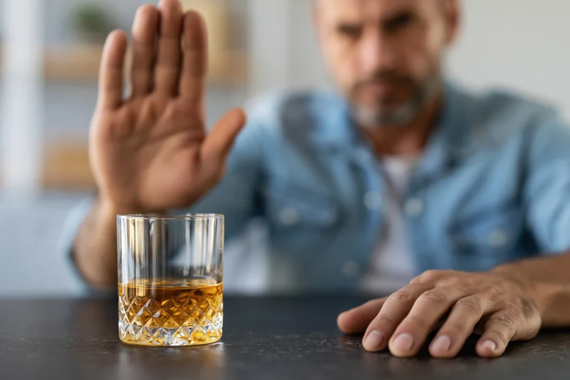 Man raising hand in refusal toward whiskey glass on dark table
