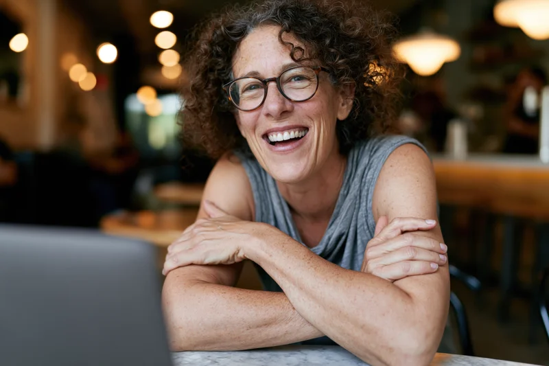 Woman smiling with arms crossed at table in cafe near laptop