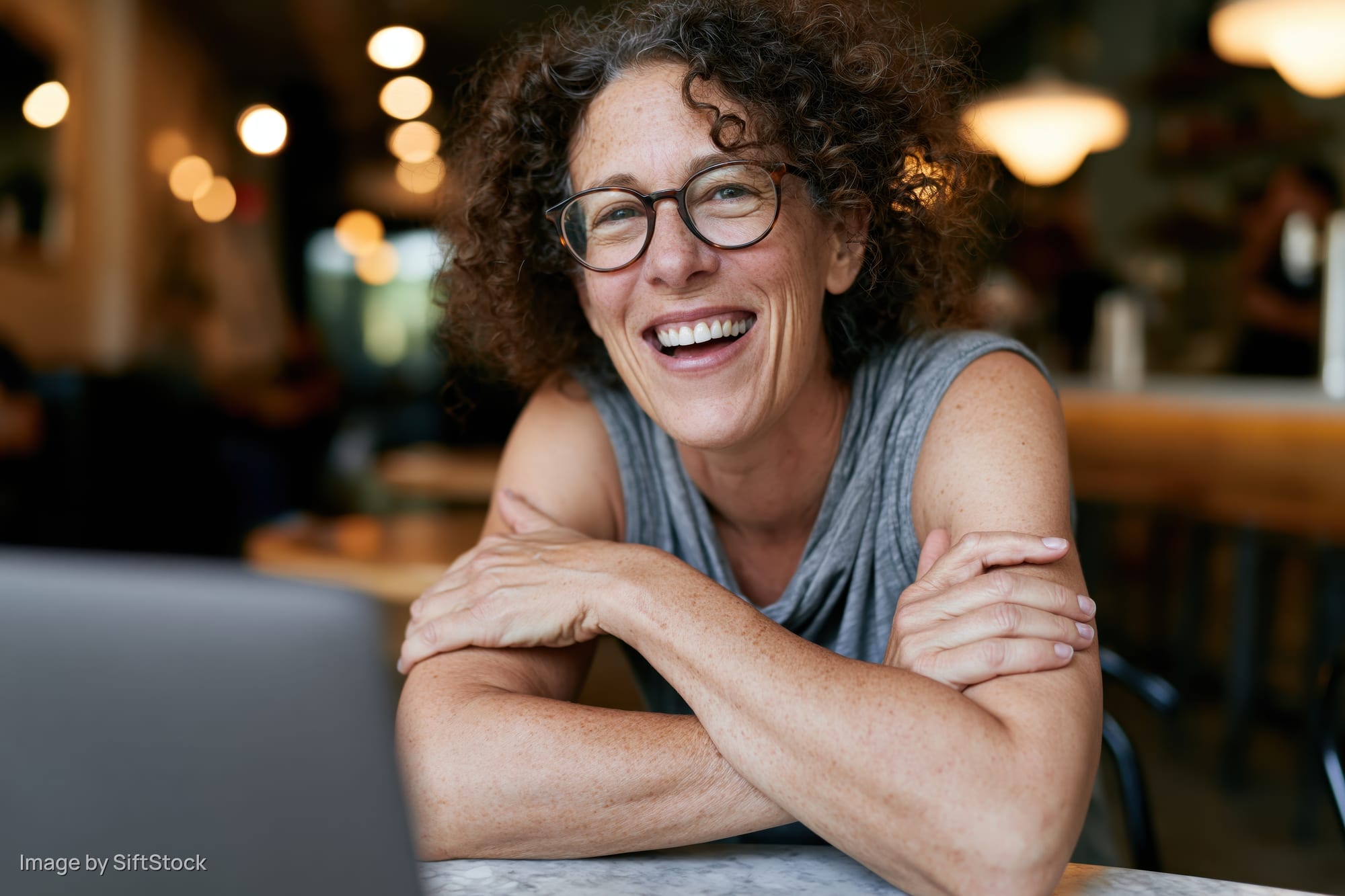 Woman smiling with arms crossed at table in cafe near laptop