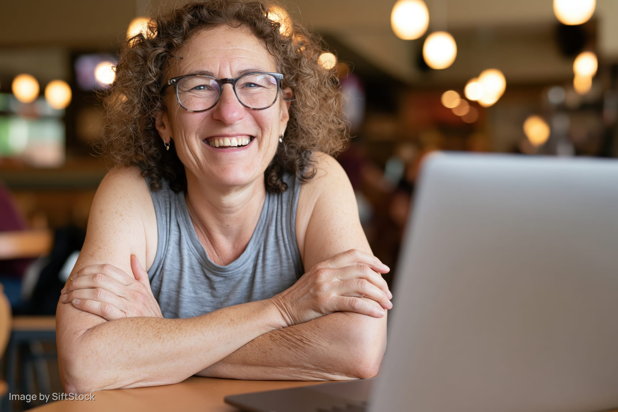 Woman smiling with arms crossed at laptop in cafe