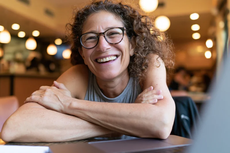 Woman smiling with arms crossed at cafe table near laptop