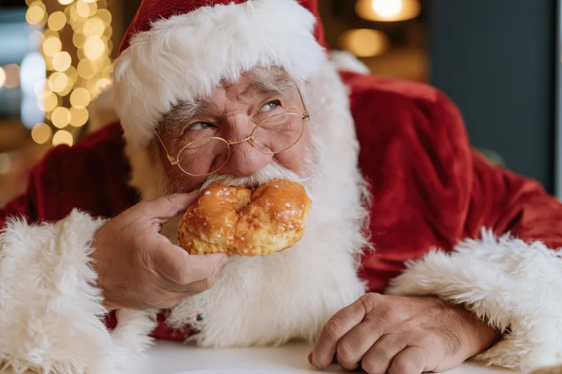 Santa eating a pastry at a cafe table with warm bokeh lights in the background