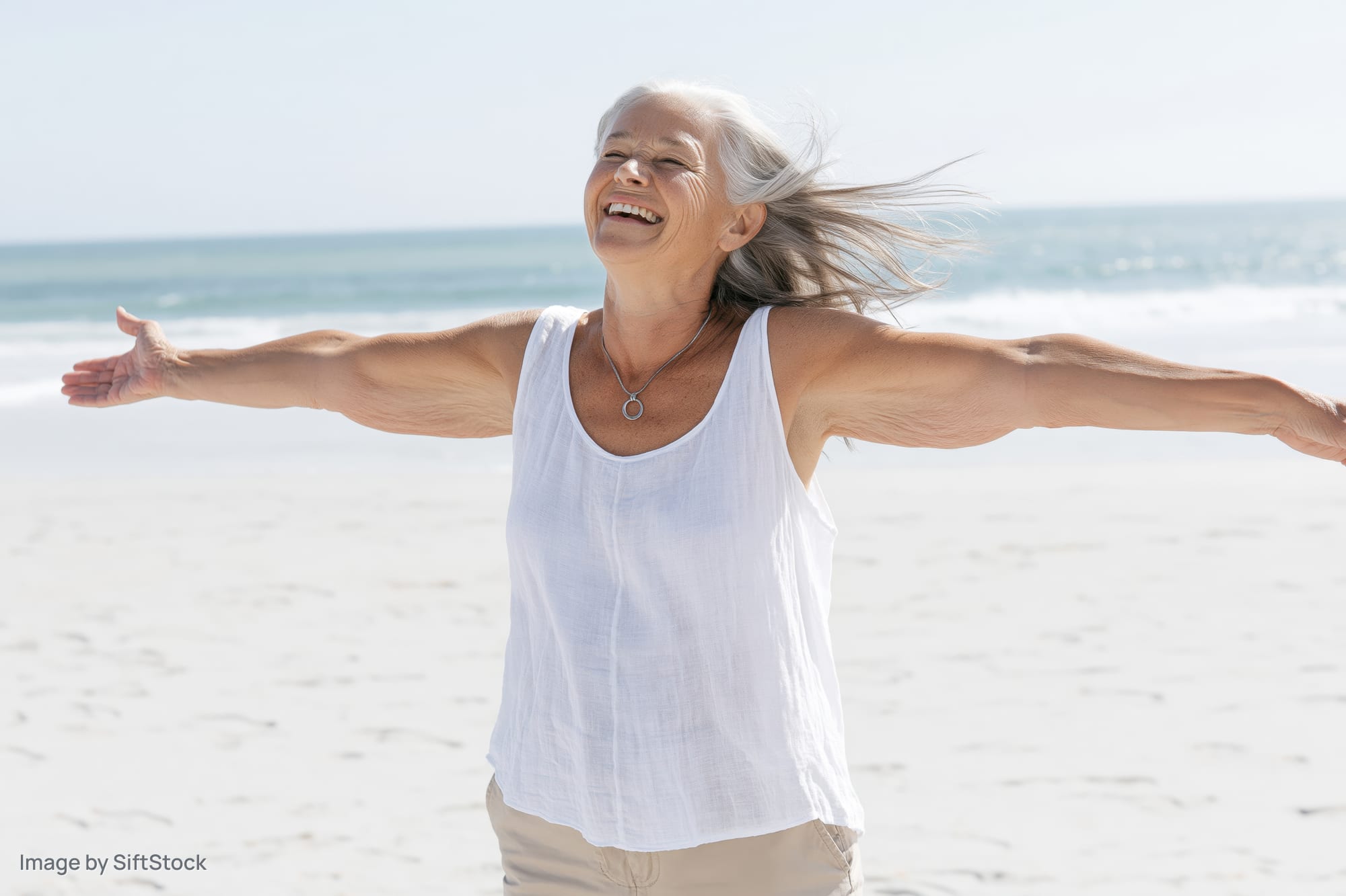 Senior woman laughing with arms outstretched on a sunny beach