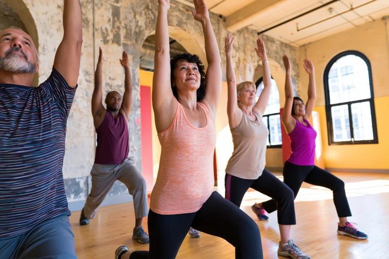 Diverse adults performing lunges with arms raised in a sunlit industrial studio