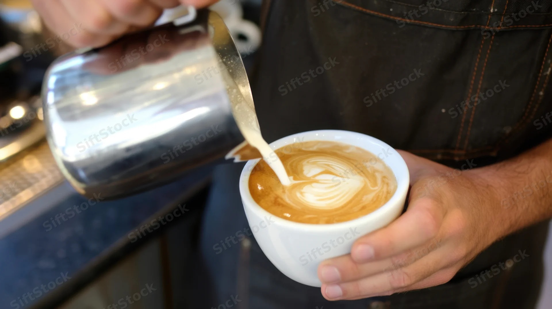 Barista pouring steamed milk into a latte cup to create foam art in a coffee shop