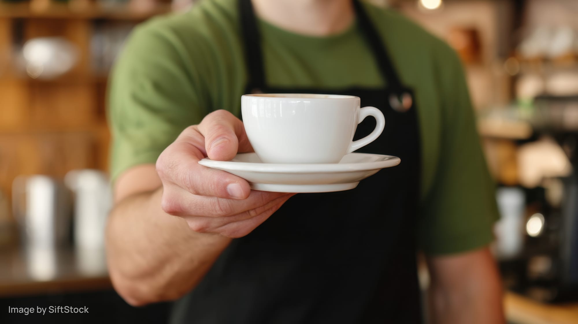 Barista holding white coffee cup and saucer in a cafe