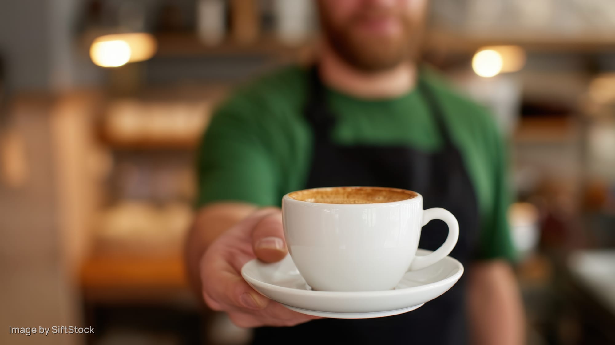 Barista holding a white ceramic coffee cup with saucer in a cafe