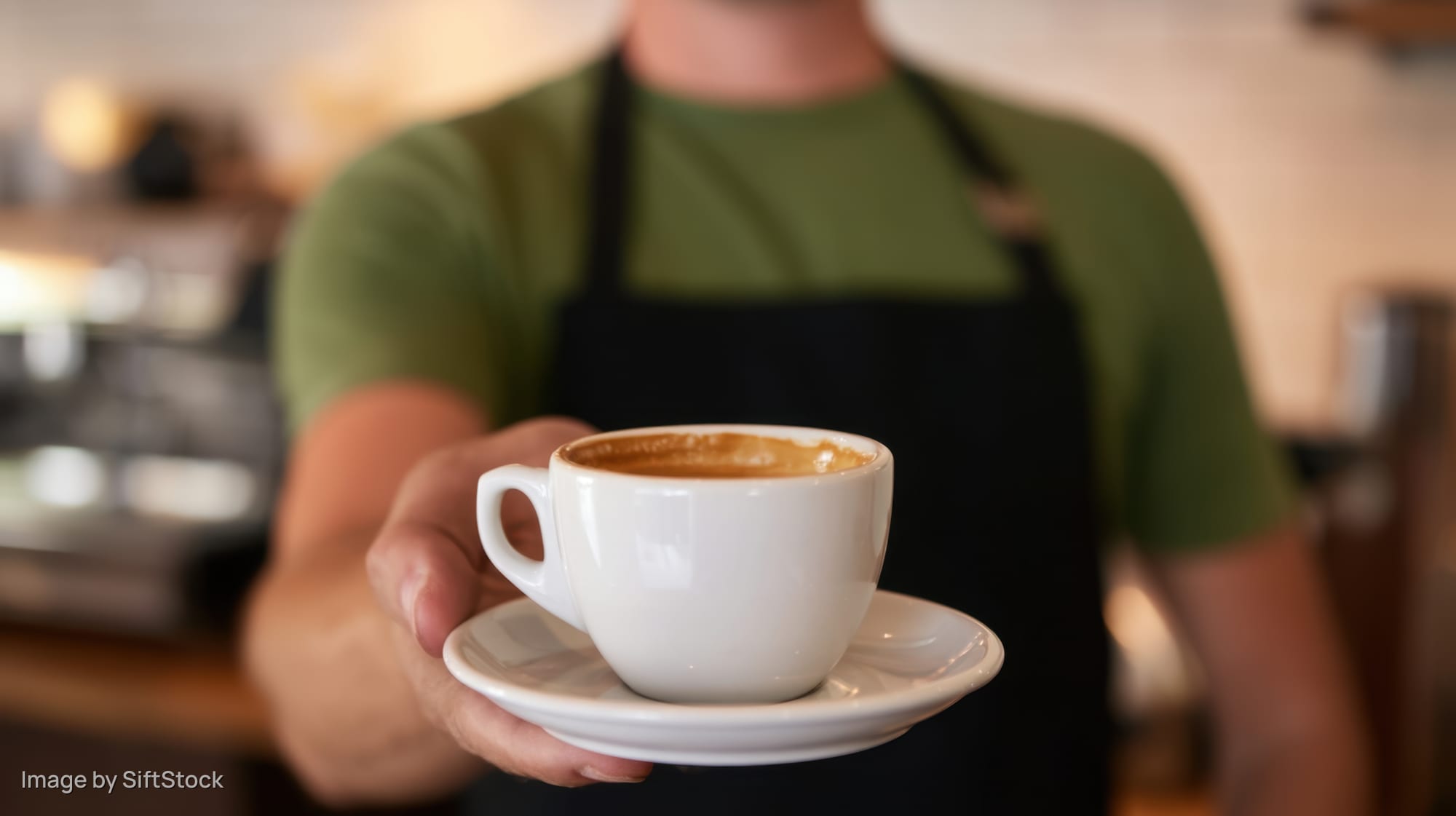 Barista holding a white ceramic coffee cup with saucer in a cafe interior