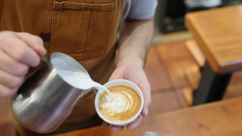 Barista pouring steamed milk into a latte cup to create foam art in a cafe
