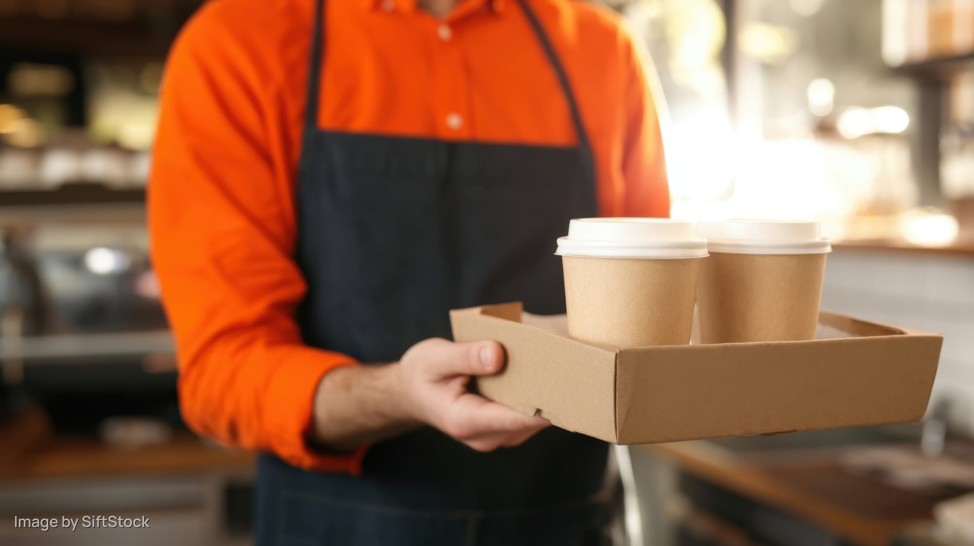 Barista holding tray with two paper coffee cups in a cafe interior