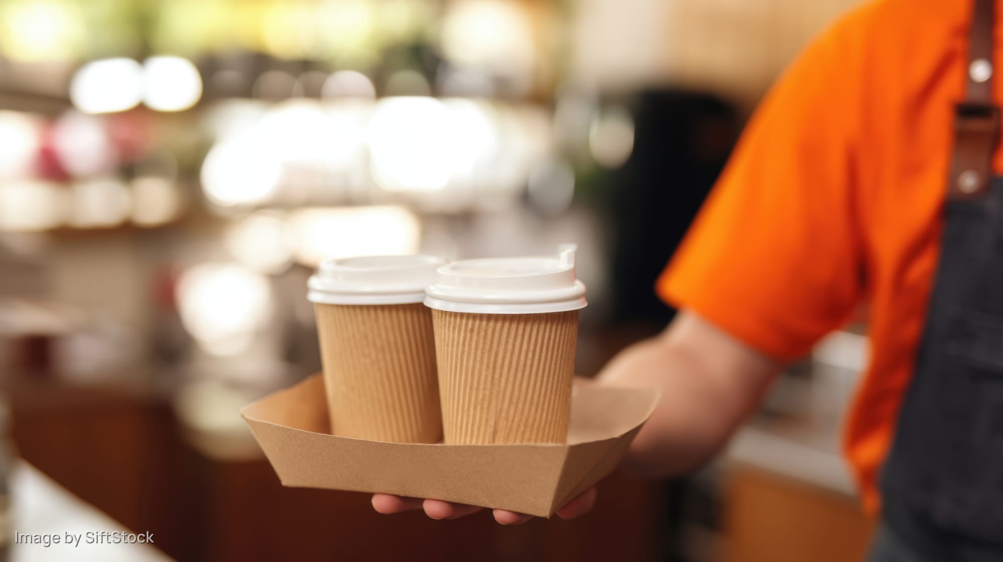 Barista holding two coffee cups in a cardboard tray in a cafe