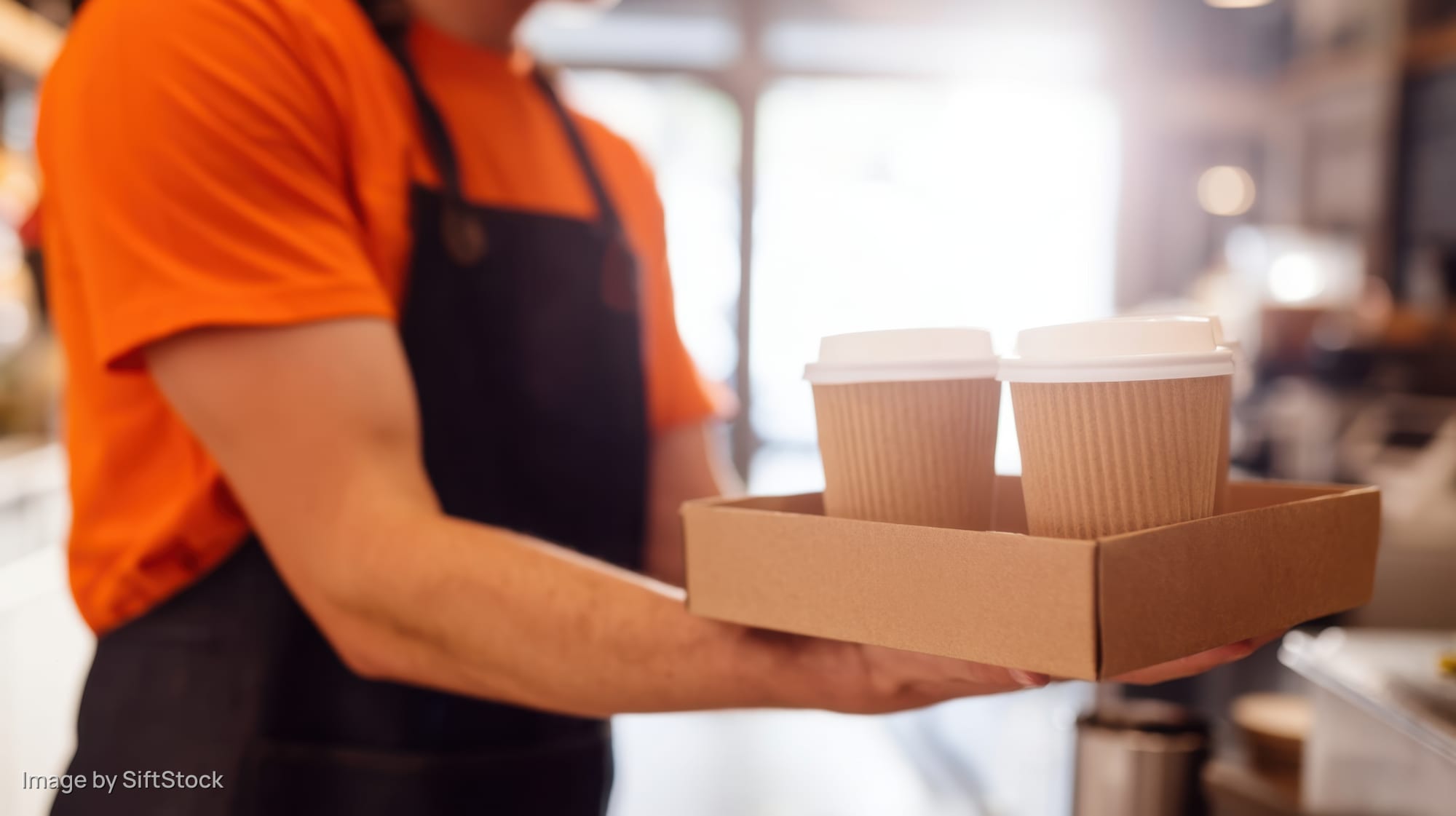 Barista holding tray with two coffee cups in a cafe