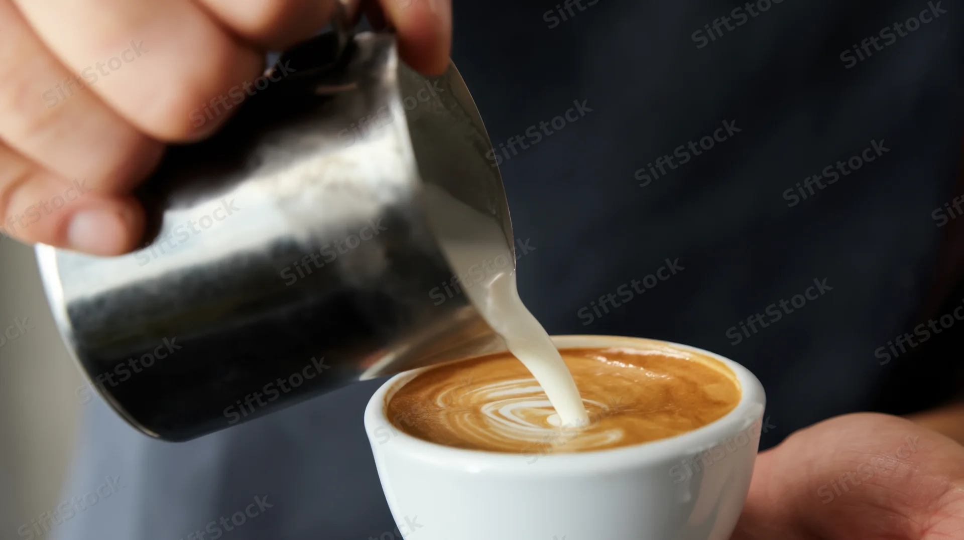 Barista pouring steamed milk into a latte cup to create foam art