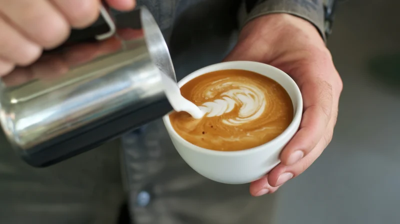 Barista pouring steamed milk into a cup of coffee to create latte art
