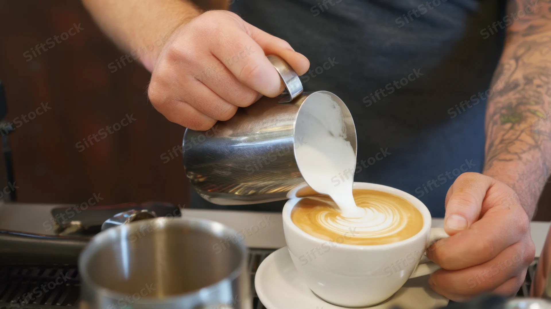 Barista pouring steamed milk into a latte cup to create foam art at a coffee counter