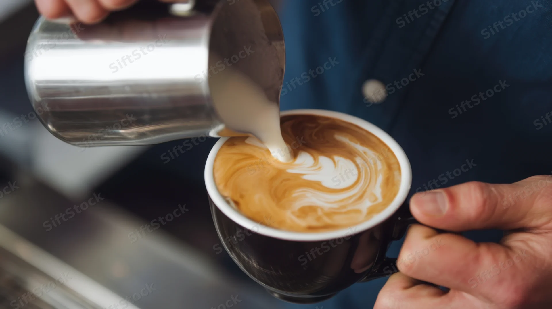 Barista pouring steamed milk into a latte to create latte art in a coffee shop