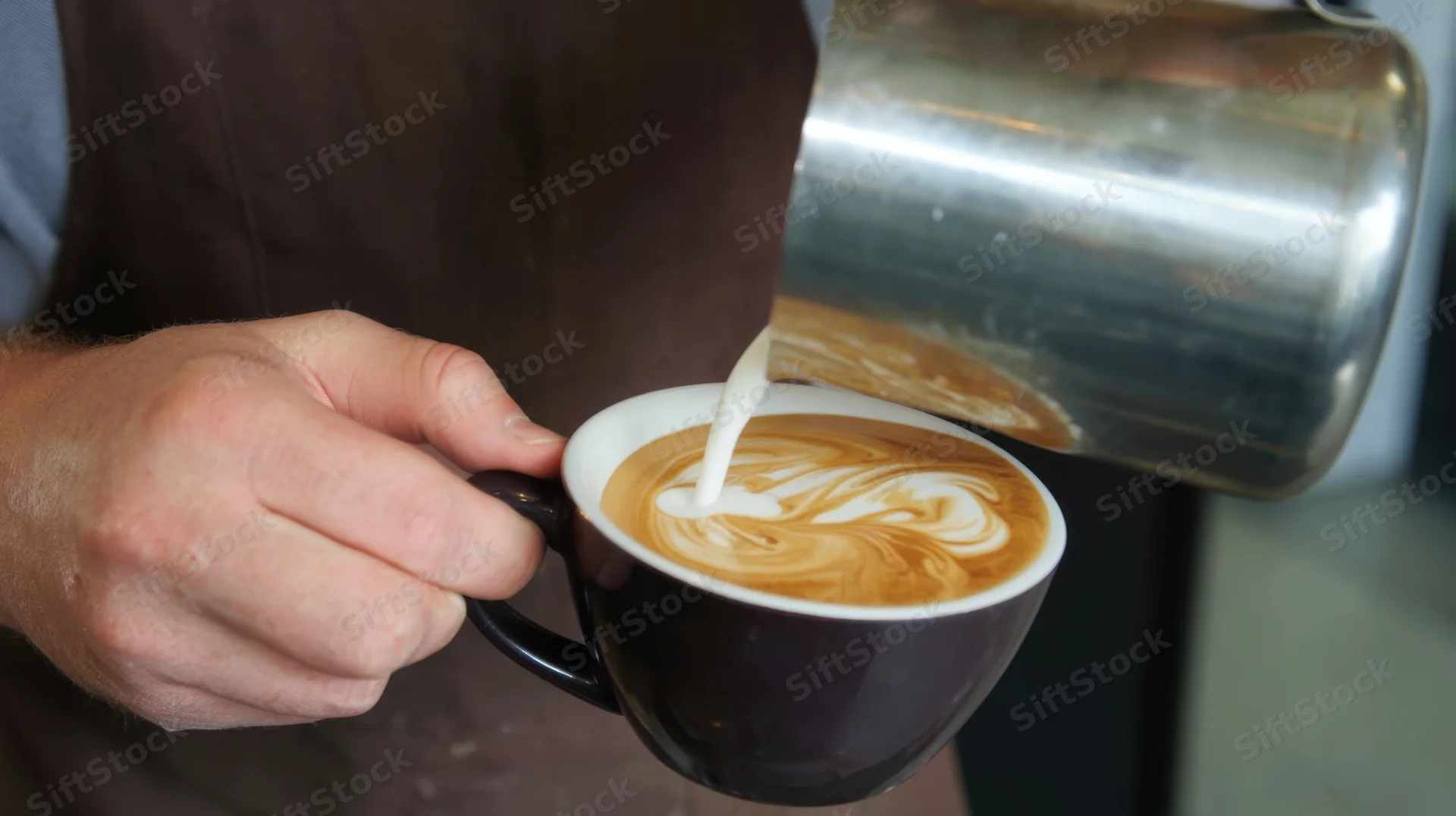 Barista pouring milk into a latte to create foam art in a ceramic cup
