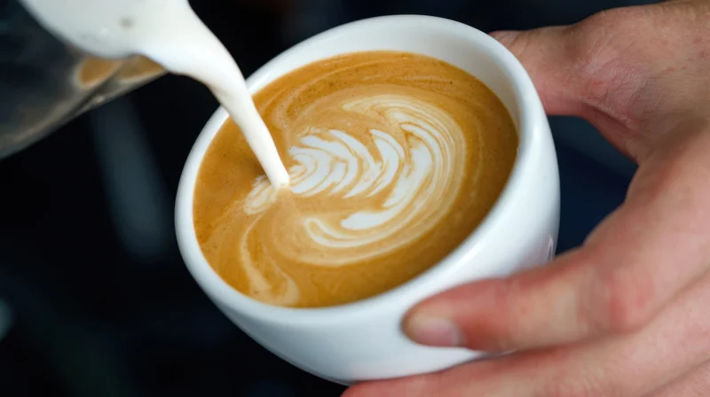 Barista pouring milk into a cup of coffee to create latte art
