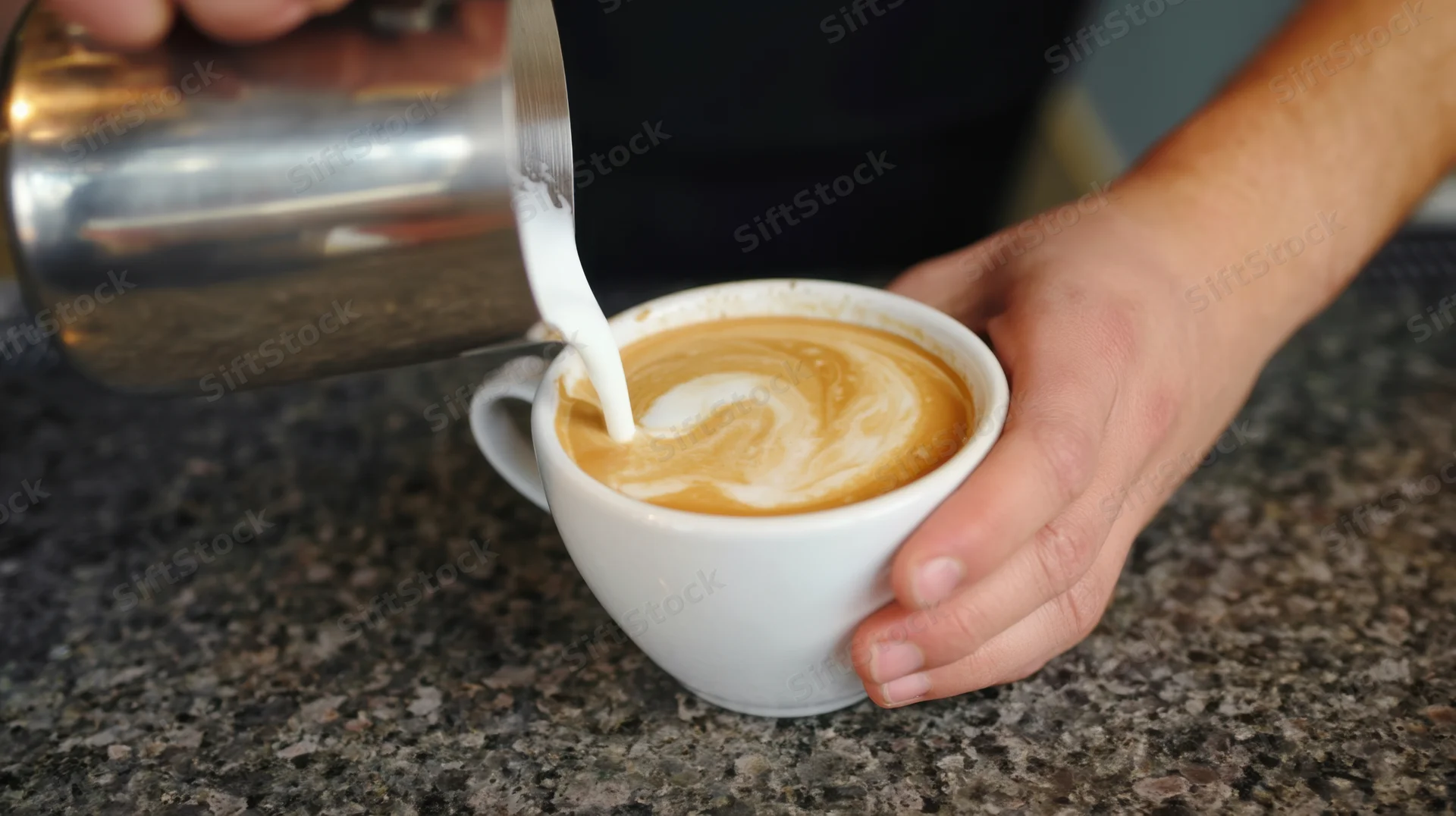 Barista pouring steamed milk into a latte cup on a granite countertop