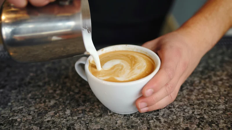 Barista pouring steamed milk into a latte cup on a granite countertop