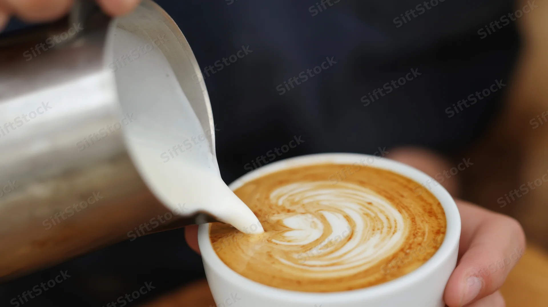 Barista pouring steamed milk into a latte cup to create foam art in a café
