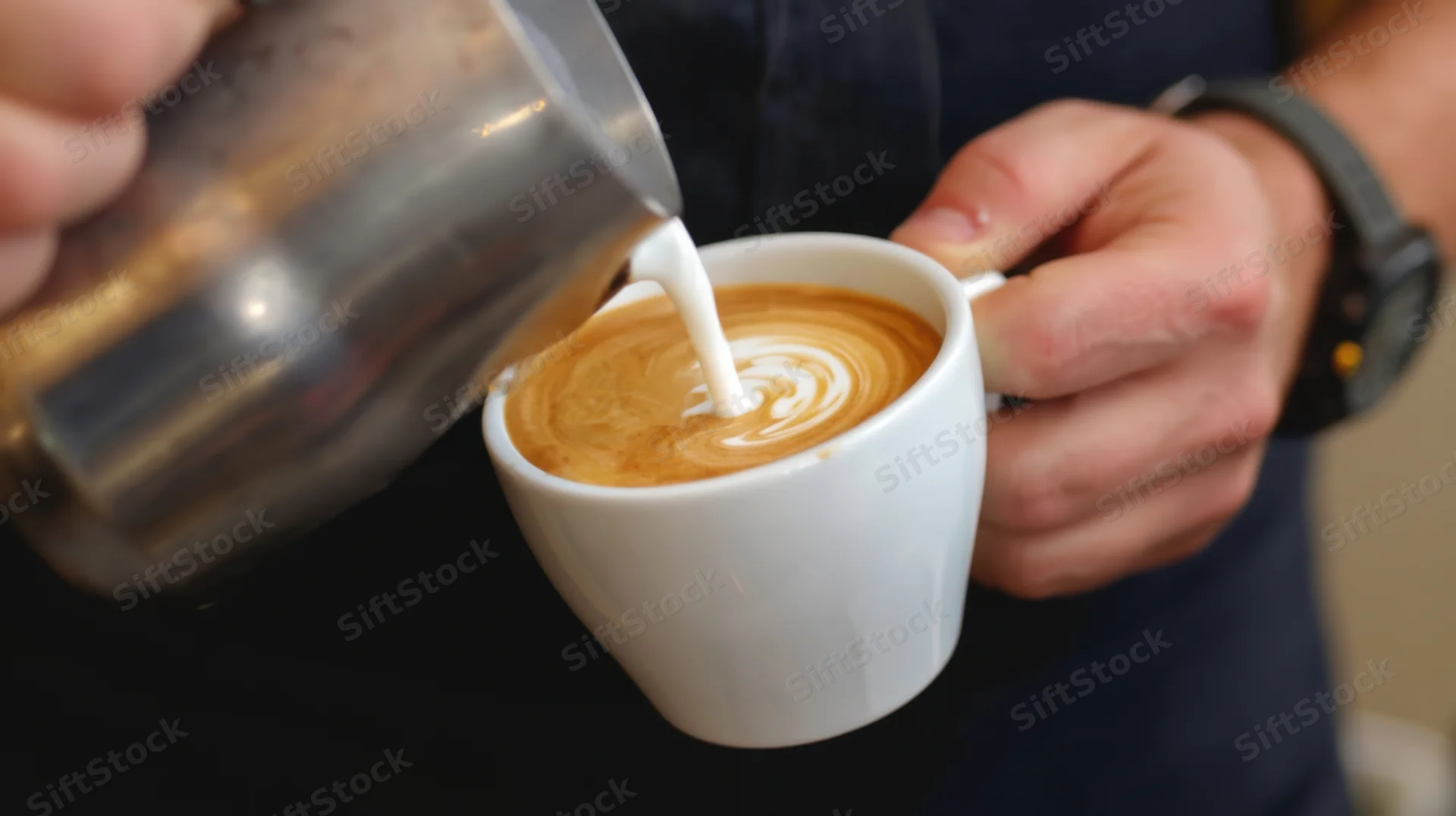 Barista pouring steamed milk into a latte cup to create foam art