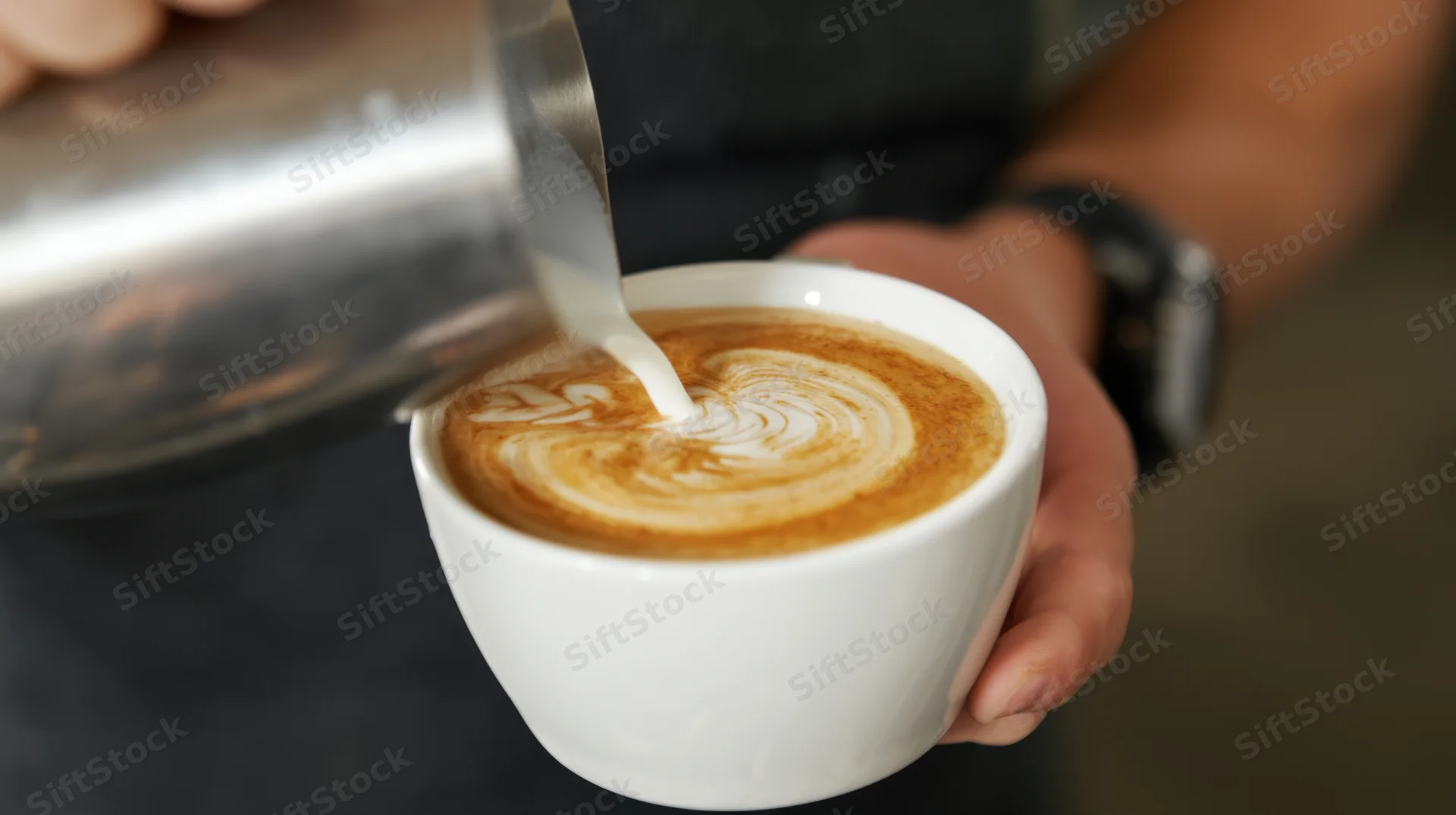 Barista pouring steamed milk into a white cup of coffee to create latte art