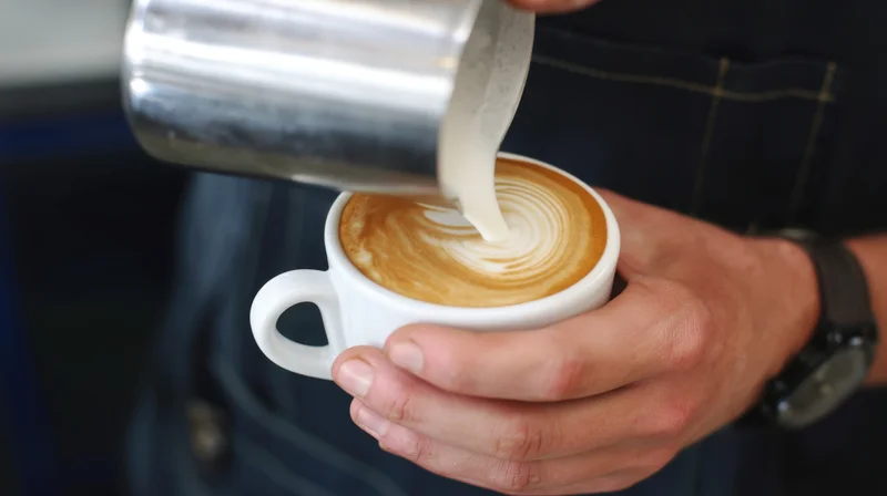 Barista pouring steamed milk into a white cup to create latte art in a cafe