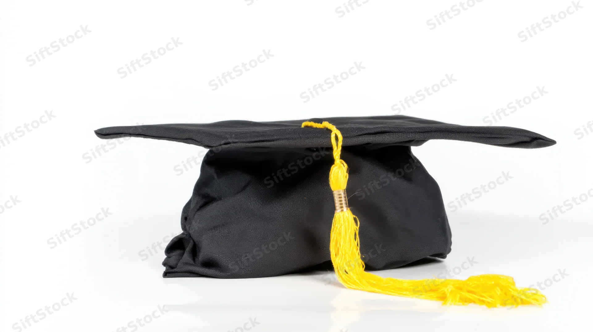 Black graduation cap with yellow tassel on white surface