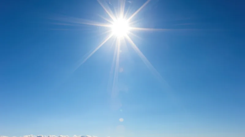 Bright sun radiating light across clear blue sky with distant clouds along horizon
