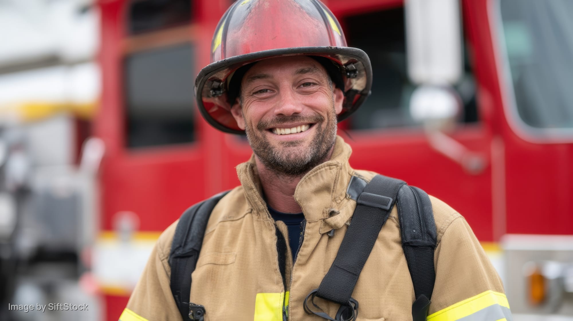 Smiling firefighter in turnout gear standing before a red firetruck