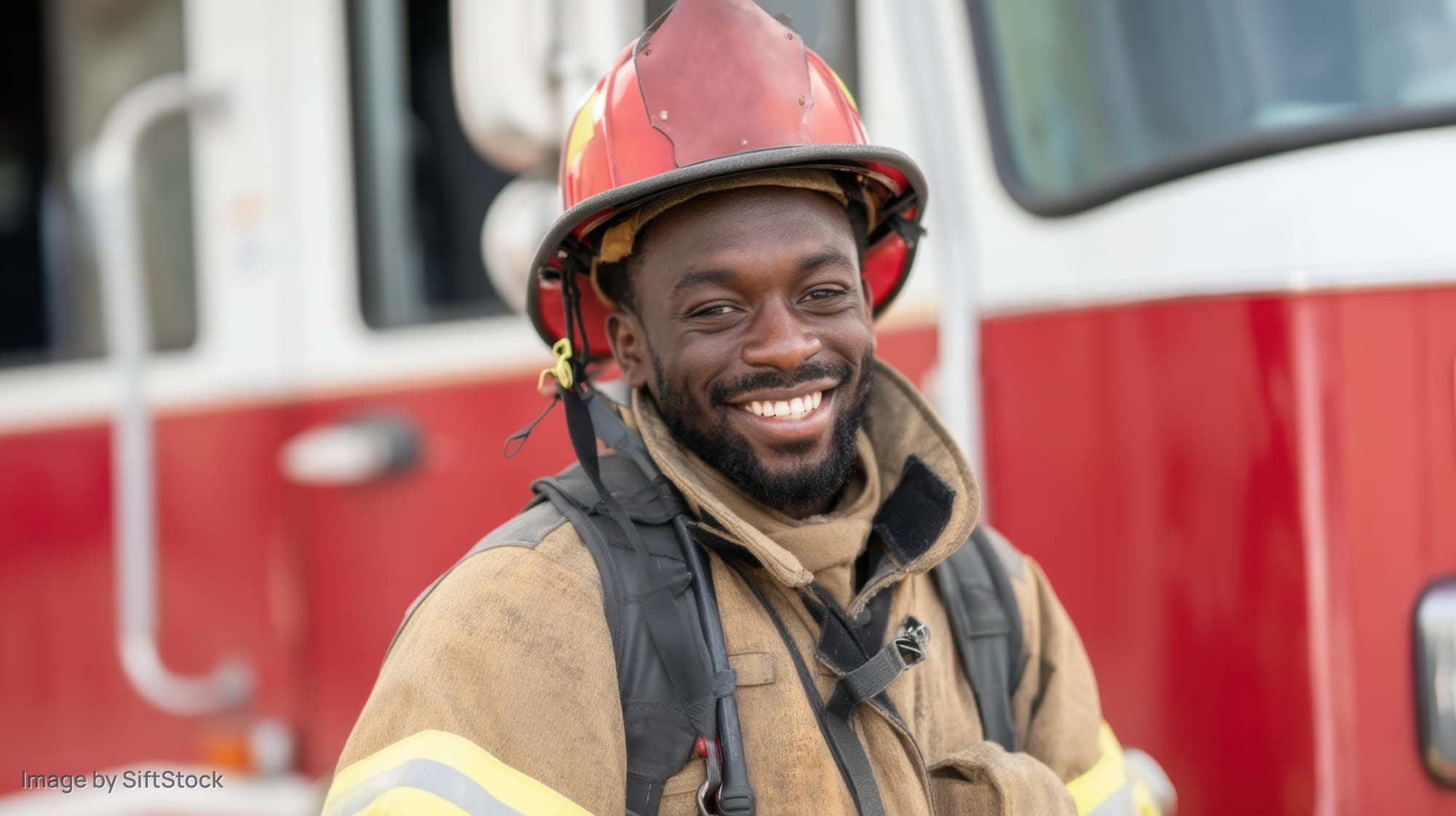Smiling firefighter in uniform standing by firetruck outdoors