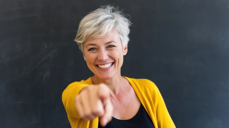 Smiling woman pointing at camera in front of blackboard