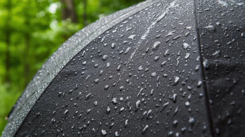 Close-up of a black umbrella covered in raindrops with green foliage in the background