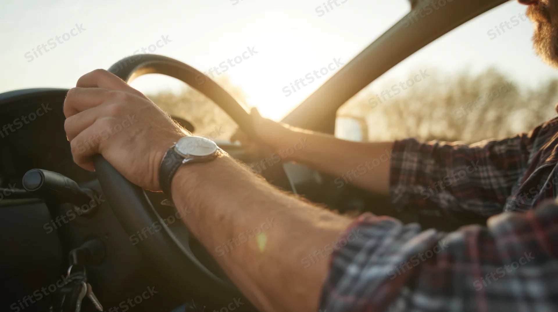 Man driving a car with hands on steering wheel, sunlight streaming through windshield