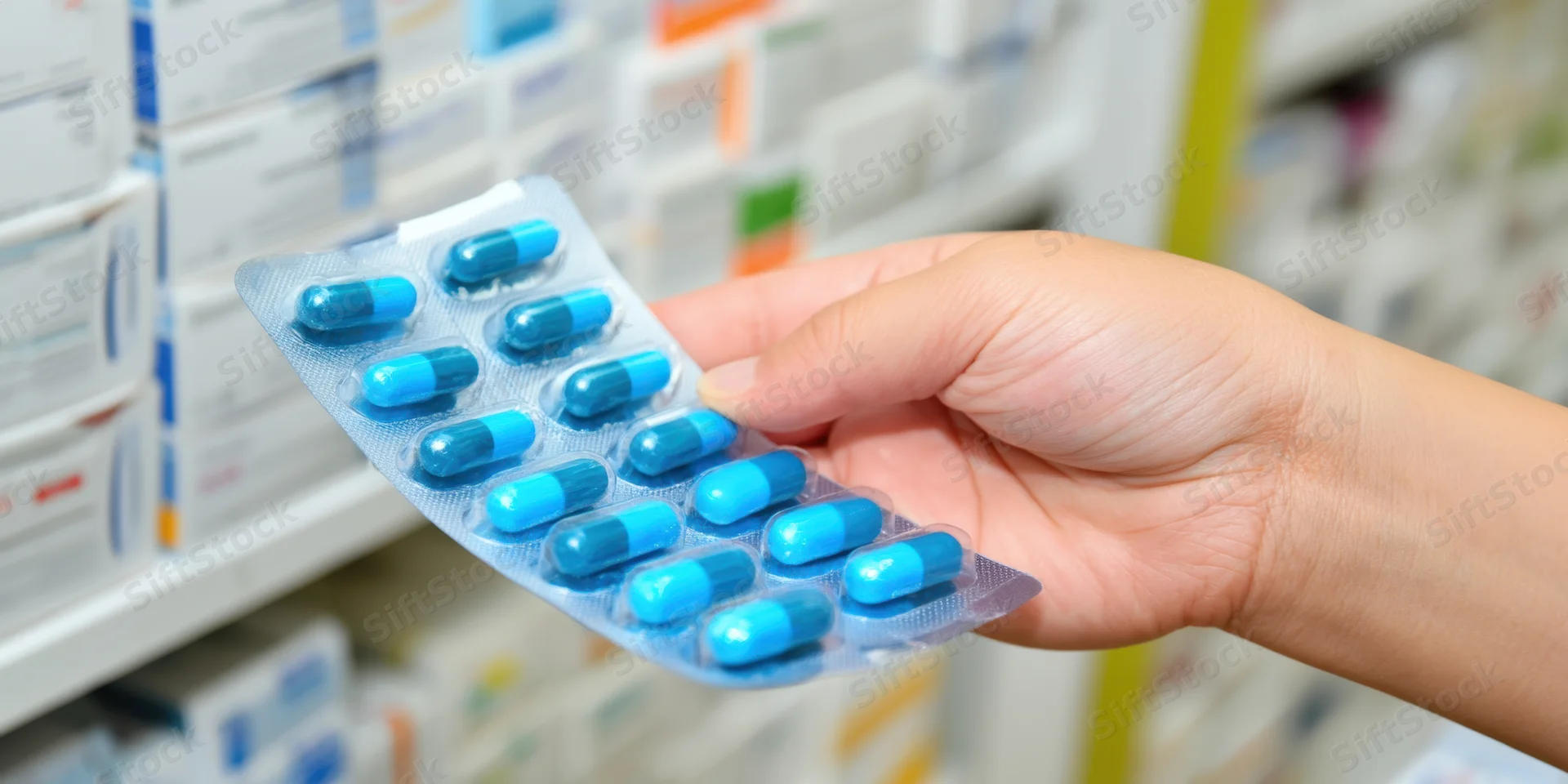 Hand holding a blister pack of blue capsules in a pharmacy setting