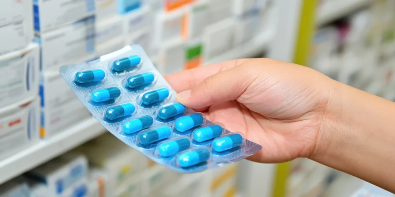 Hand holding a blister pack of blue capsules in a pharmacy setting