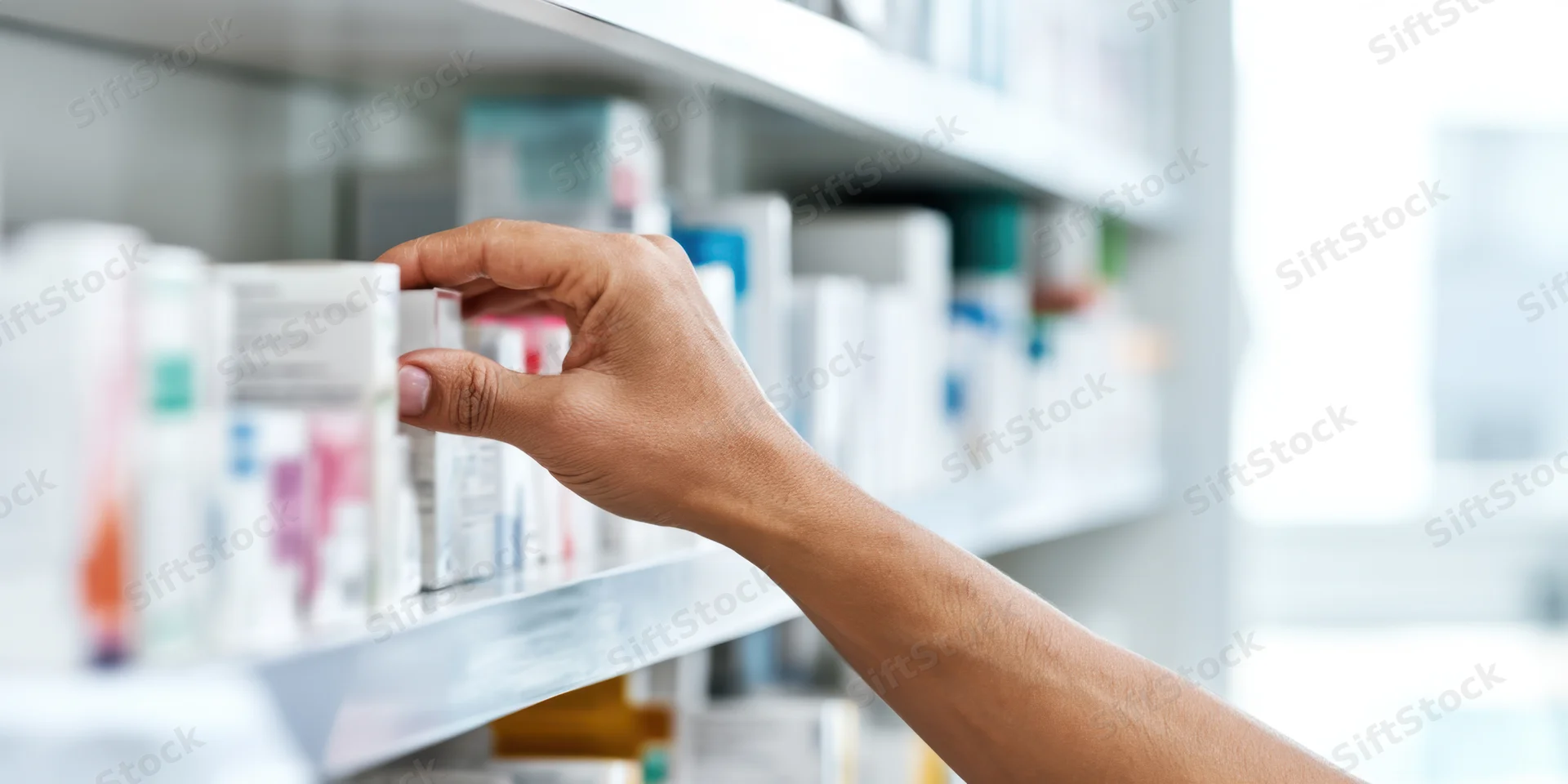 Hand reaching for medication box on pharmacy shelf
