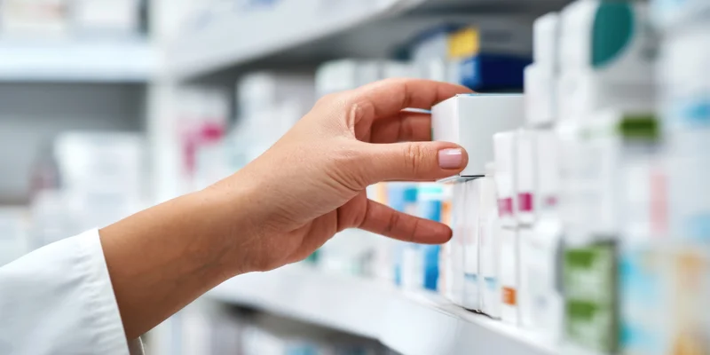 Pharmacist's hand selecting medication box from pharmacy shelf