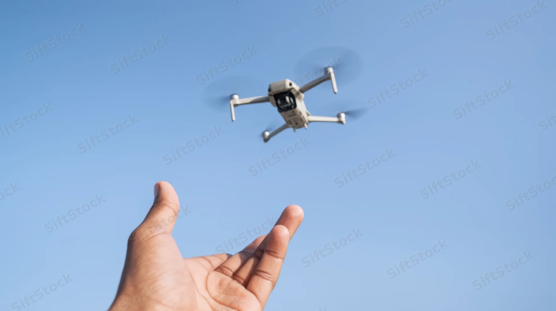 Hand gesturing toward a flying drone against a clear blue sky