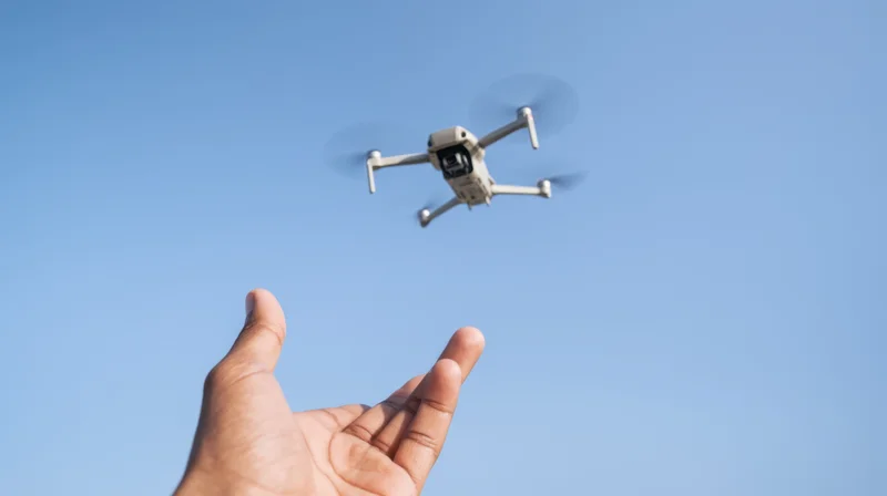 Hand gesturing toward a flying drone against a clear blue sky