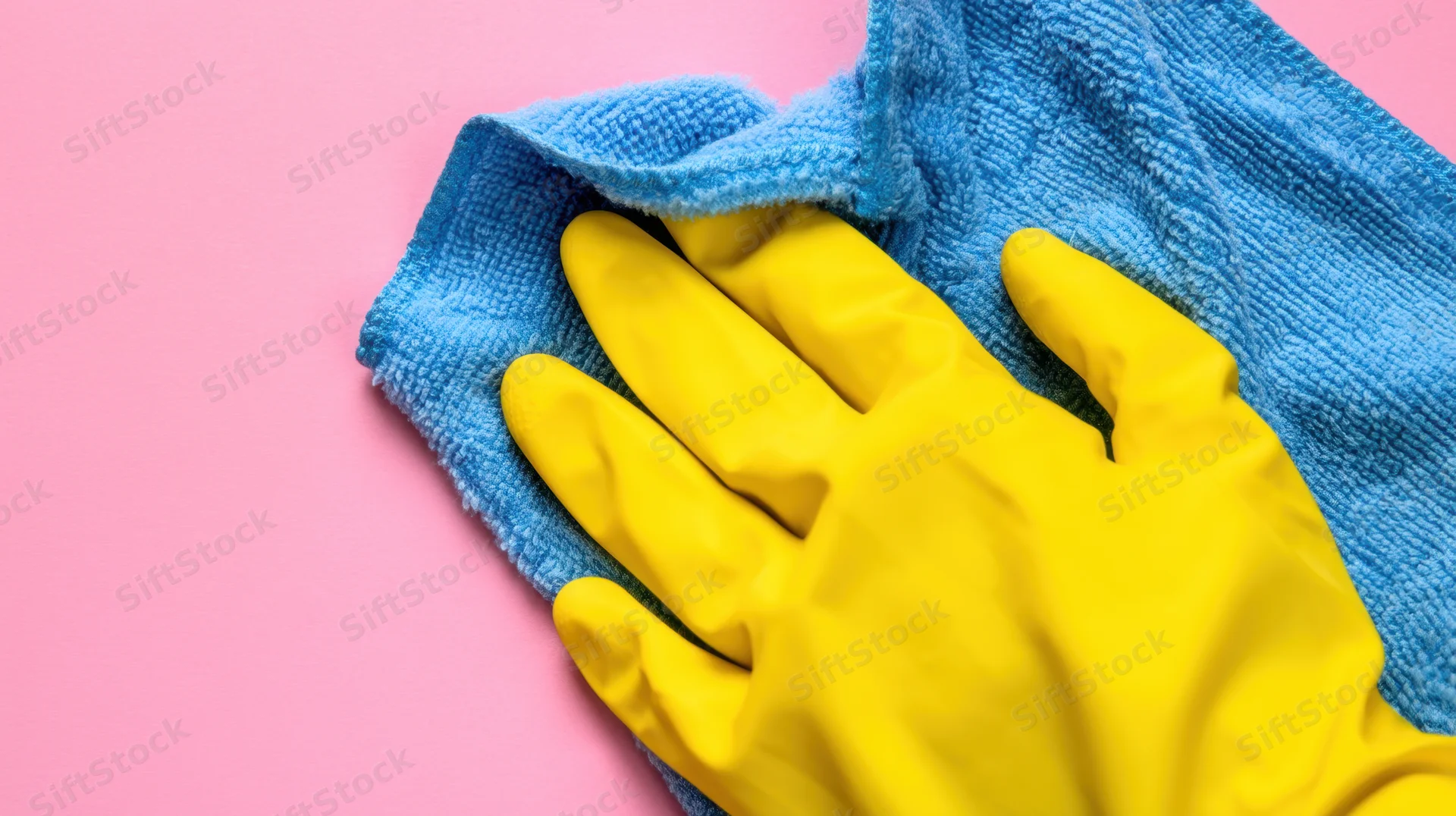 Yellow rubber glove resting on blue towel against pink background