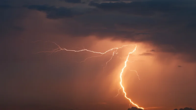 Lightning striking across a stormy night sky with dark clouds and orange glow
