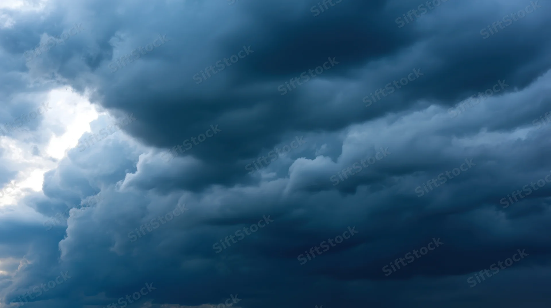 Dark storm clouds filling the sky with light breaking through on the left