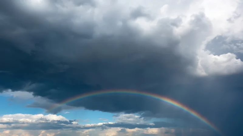 Rainbow arching across stormy sky with dark clouds and patches of blue