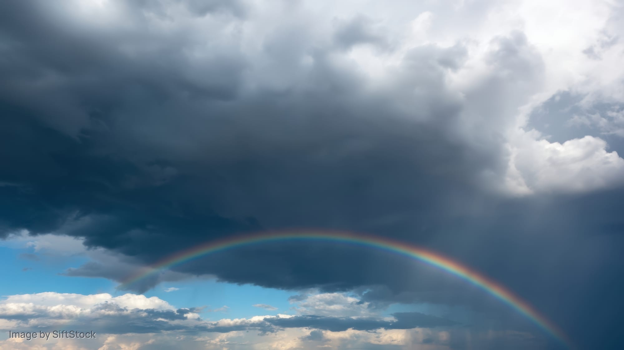 Rainbow arching across stormy sky with dark clouds and patches of blue