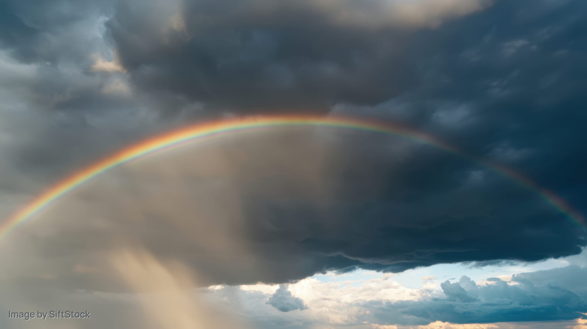 Rainbow arching across stormy sky with dark clouds and patches of light