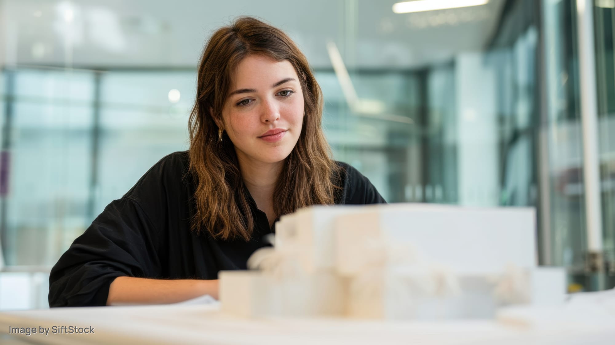 Woman examining architectural model at desk in modern office